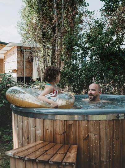 Ein Vater und sein Kind genießen gemeinsam die Zeit im Whirlpool. Die Umgebung ist grün und einladend.