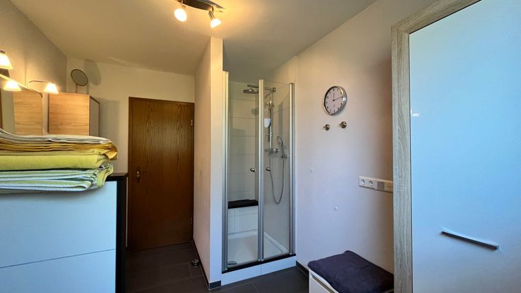 Ein modernes Badezimmer mit einer Dusche und einem Waschbecken. Der Raum ist hell und gut organisiert, mit einem Schrank und einer Uhr an der Wand.