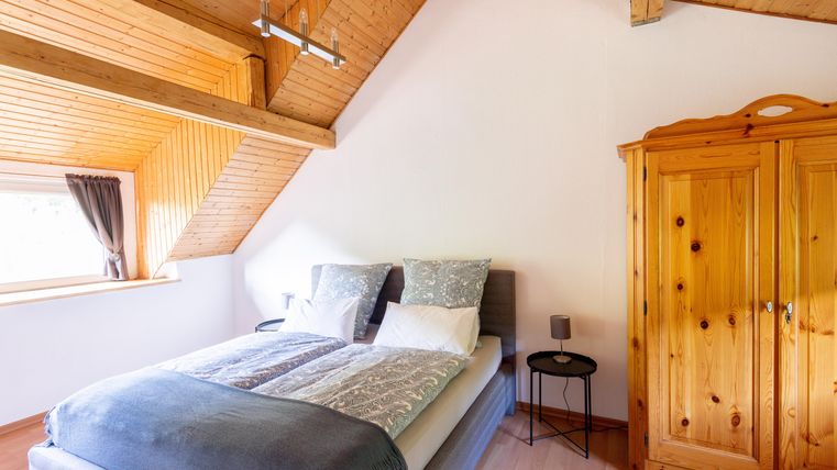 A cozy bedroom with a double bed and wooden paneling. A wooden wardrobe and a small nightstand complement the furnishings.