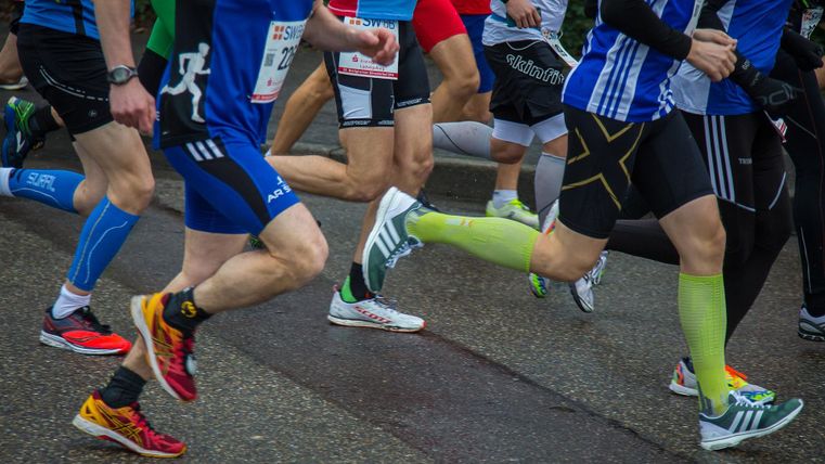 Eine Gruppe von Läufern in Sportkleidung bewegt sich schnell auf der Straße. Die Füße und Beine der Teilnehmer sind deutlich sichtbar, während sie an einem Wettlauf teilnehmen.