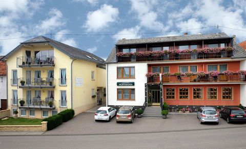 Ein kleines Hotel mit zwei Gebäuden und Balkonen. Vor dem Hotel stehen einige Autos und der Himmel ist teilweise bewölkt.