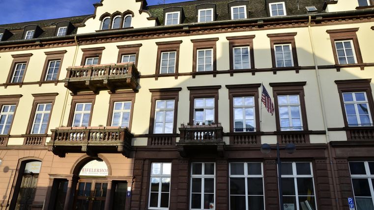 Ein historisches Gebäude mit mehreren Fenstern und Balkonen. Die Fassade ist in einem gelben Farbton gehalten und es gibt eine Fahne sichtbar.