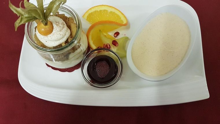 Une assiette à dessert avec un verre de douceur, décorée de crème et d'un fruit des bois. À cela s'ajoute une sauce à la vanille et des fruits frais comme l'orange et le kiwi.