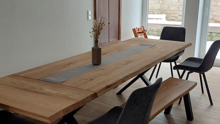 Een moderne eetruimte met een grote houten tafel en elegante stoelen. Een stijlvolle lamp hangt boven de tafel, de ruimte voelt licht en uitnodigend aan.