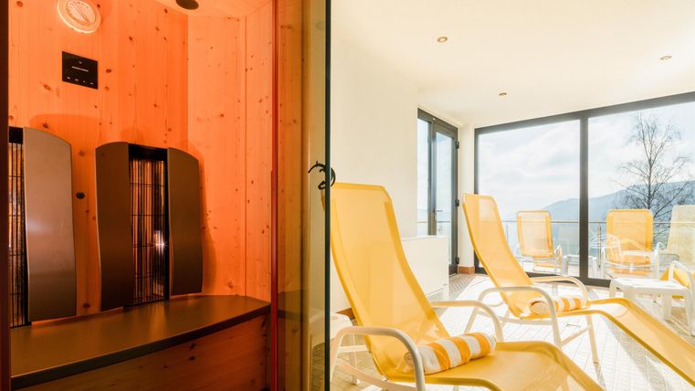 Eine moderne Sauna auf der linken Seite und ein entspannender Ruheraum mit Liegen auf der rechten Seite. Große Fenster bieten einen Blick auf die Natur.