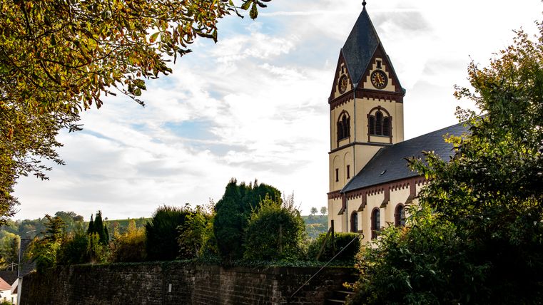 Kirche St. Remigius in Oberweis, umgeben von Bäumen und einer Steinmauer.