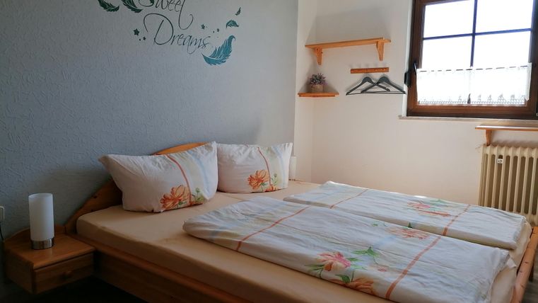 Ein gemütliches Schlafzimmer mit einem großen Bett und künstlerischen Wänden. Der Raum hat ein Fenster mit Tageslicht und schlichte Möbel.