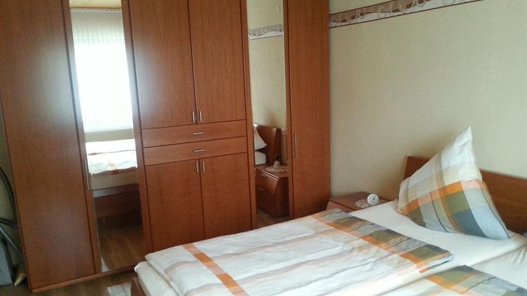 Une chambre simple avec un lit double et une grande armoire. La pièce a des murs clairs et beaucoup de lumière naturelle.