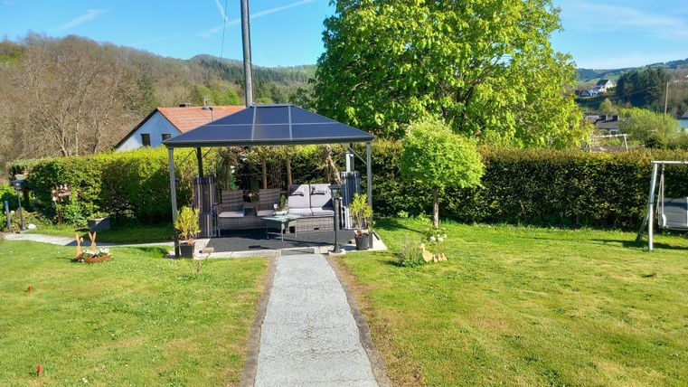 A cozy garden landscape with a gazebo and plenty of greenery. The path leads to the gazebo, surrounded by plants and trees.