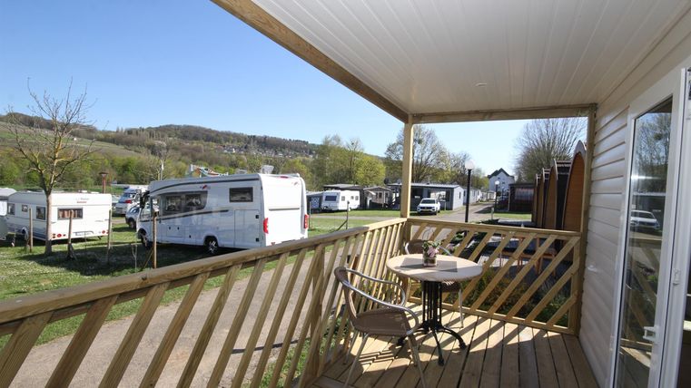 Eine Terrasse mit einem Tisch und Stühlen, die einen schönen Blick auf einen Campingplatz bietet. Im Hintergrund sind Wohnmobile und grüne Hügel zu sehen.