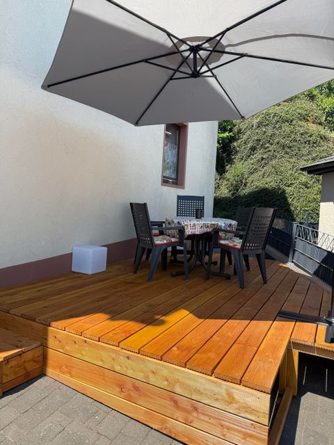 A cozy terrace with a wooden deck and a large sun umbrella. A round table with chairs invites you to linger.
