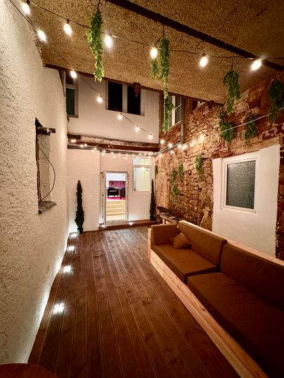 Un cour intérieure confortable avec un sol en bois et un banc douillet. Des lumières discrètes et des plantes créent une atmosphère accueillante.