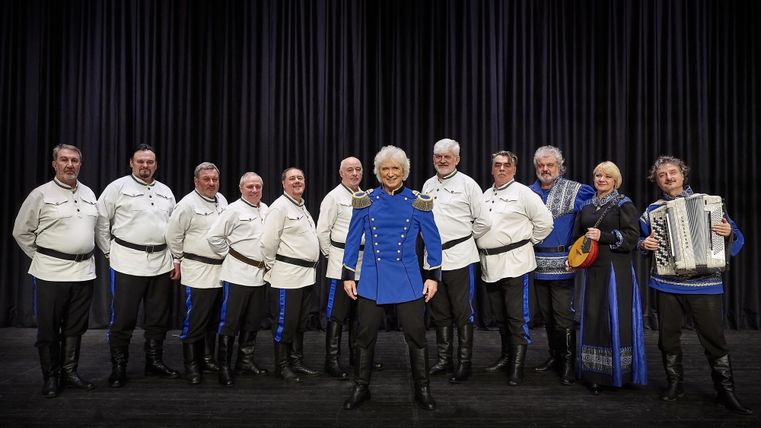 Eine Gruppe von Personen in traditionellen Trachten steht gemeinsam auf einer Treppe. Sie lächeln und posieren für das Foto.
