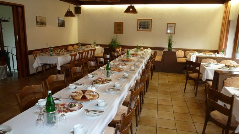 Ein einladender Speisesaal mit langen Tischen, die mit verschiedenen Gerichten und Getränken gedeckt sind. Die Atmosphäre ist gemütlich mit Holzstühlen und warmem Licht.