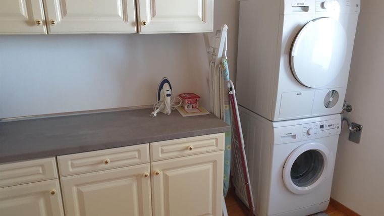 Une salle de lavage fonctionnelle avec un lave-linge et un sèche-linge. Sur le plan de travail se trouvent un fer à repasser et quelques ustensiles.