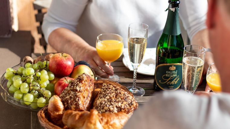 Ein Tischgedeck mit frischem Obst, Brötchen und Sekt. Im Hintergrund sind Gläser mit Saft und Sekt zu sehen.