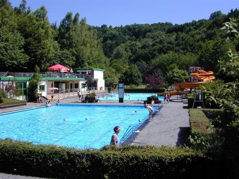 Ein schöner Schwimmbereich mit zwei Pools und einer Rutsche. Die Umgebung ist grün und einladend.
