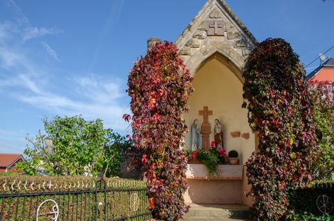 Eine kleine Kapelle mit Statuen und roten Kletterpflanzen in Wolsfeld.