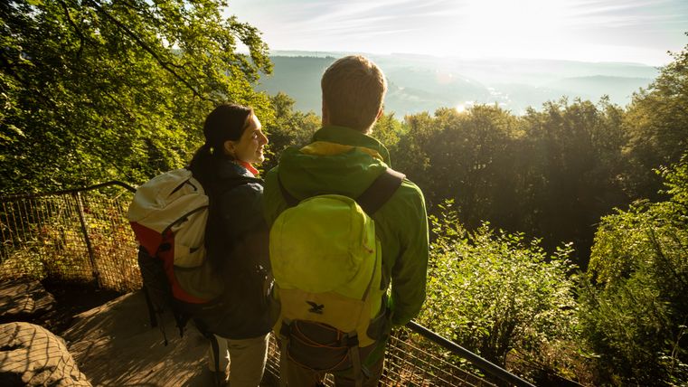 Zwei Wanderer mit Rucksäcken genießen die Aussicht von einem Aussichtspunkt im Wald.