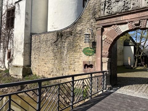 Un bâtiment historique avec une belle façade en pierre et une porte romantique. Un pont traverse un petit ruisseau menant à l'entrée.