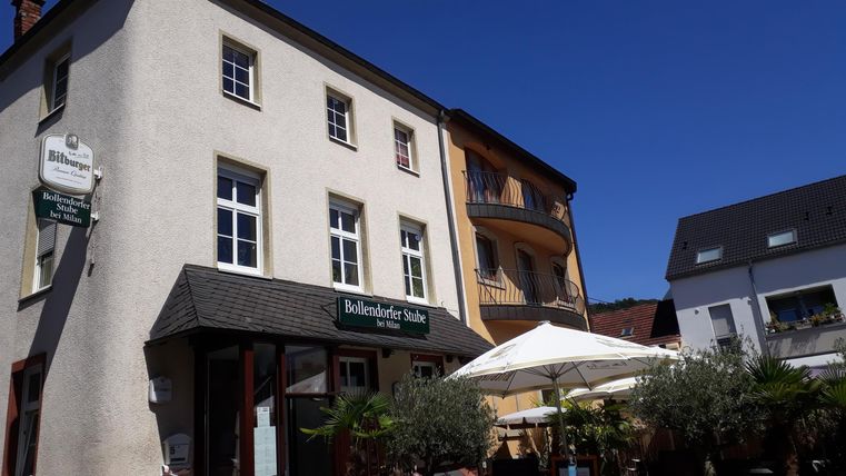A charming building with several windows and an entrance. There are sun umbrellas and plants in front of the house.