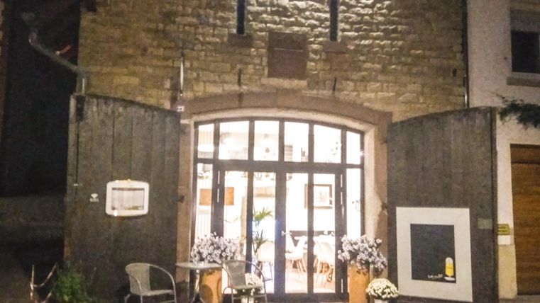 Een mooi verlicht gebouw met grote ramen en een uitnodigende ingang. Voor het gebouw staan ​​tafels en stoelen om een gezellige buitenruimte te creëren.