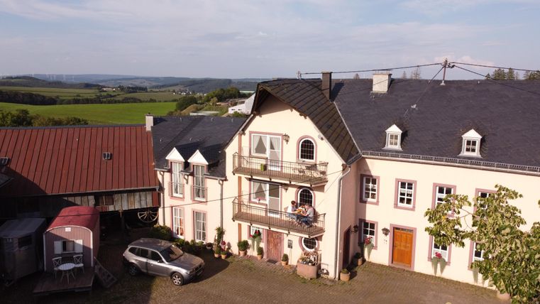 Ein landwirtschaftliches Gebäude mit einem schönen, großen Hof. Im Hintergrund sind grüne Felder und ein blauer Himmel zu sehen.