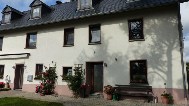 Un bel appartement à deux étages avec un espace extérieur lumineux. Devant la maison, des fleurs sont présentes et un banc invite à la détente.