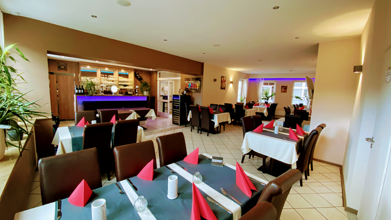 Un restaurant accueillant avec un décor élégant. Les tables sont dressées avec des nappes blanches et des serviettes rouges.