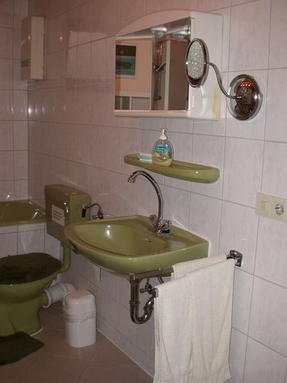 Ein kleines Badezimmer mit einer grünen Waschbecken und Toilette. An der Wand hängt ein Spiegel und ein Handtuch ist aufgehängt.