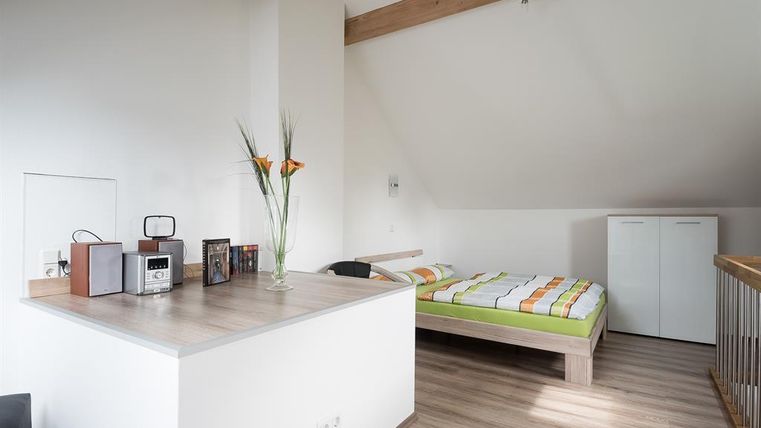 Une chambre moderne avec un lit et un petit coin cuisine. Des murs clairs et des détails en bois donnent à l'espace une atmosphère chaleureuse.