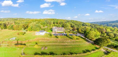 Eine malerische Landschaft mit sanften Hügeln und greenery. Im Vordergrund steht ein charmantes Gebäude, umgeben von Bäumen und einer klaren blauen Himmel.