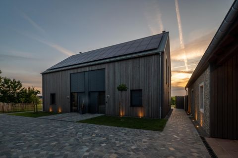 Ein modernes, zweigeschossiges Holzhaus mit großen Fenstern und einer Solaranlage auf dem Dach. Der Sonnenuntergang sorgt für eine stimmungsvolle Atmosphäre im Außenbereich.