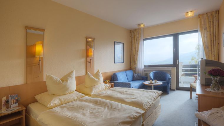 Ein helles Hotelzimmer mit zwei Betten und einem gemütlichen Sitzbereich. Große Fenster bieten einen Blick auf die Umgebung.