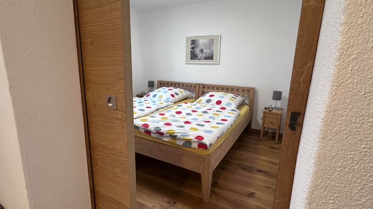 Ein einfaches Schlafzimmer mit zwei Betten und bunten Bettbezügen. Der Raum hat einen warmen Holzfußboden und eine gemütliche Atmosphäre.