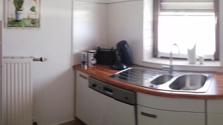 Eine moderne Küche mit weißen Schränken und einer Holzarbeitsfläche. Ein Fenster sorgt für Tageslicht und Blick nach draußen.