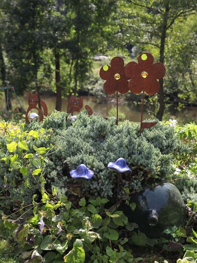 Un jardin coloré avec des plantes vertes et des fleurs bleues. Des ornements floraux en métal se tiennent au premier plan.