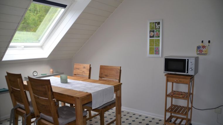 A bright dining area with a wooden table and chairs. A window lets in a lot of light, and a microwave sits on a small table.