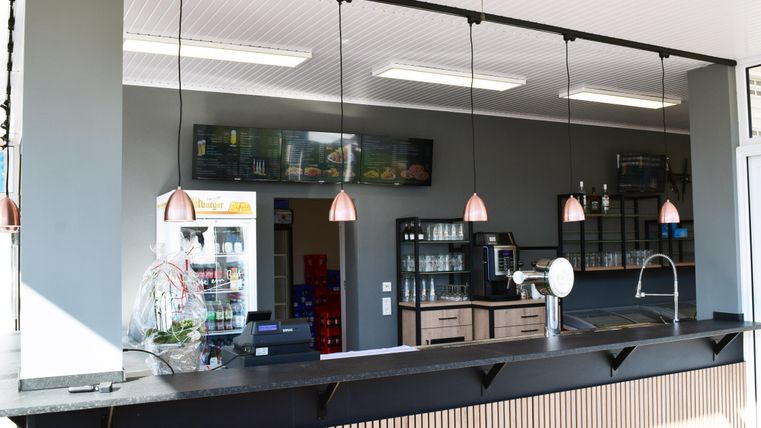 Une zone de caisse moderne avec des lampes suspendues et un design clair et épuré. En arrière-plan, quelques appareils et étagères sont visibles.