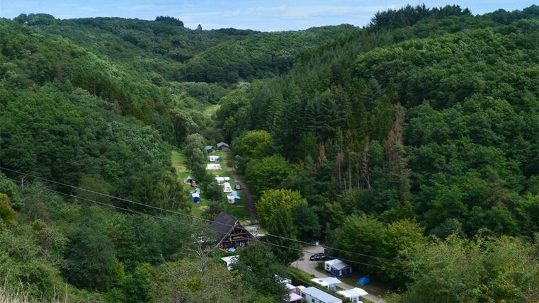 A picturesque landscape with a valley surrounded by dense forests. In the middle, campsites and a small accommodation are visible.
