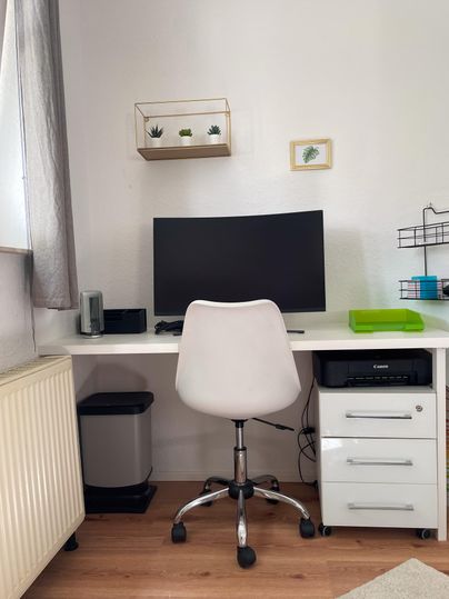 Een moderne bureau met een computerscherm en een witte bureaustoel. Een printer is ook aanwezig.