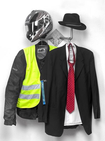 Un casque de moto et une veste de couleur fluo pendent à côté d'un costume formel avec un nœud papillon et un chapeau. Cette combinaison montre un contraste entre la tenue de loisirs et la tenue de soirée.