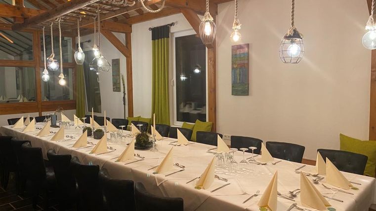 Une salle à manger élégante avec une longue table, joliment dressée. Une lumière chaude provenant de lampes suspendues crée une atmosphère accueillante.