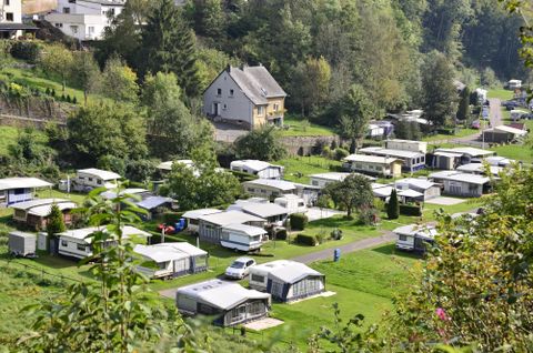 Eine ruhige Wohnsiedlung mit Wohnwagen in einer grünen Umgebung. In der Mitte steht ein kleines Haus, umgeben von Bäumen und Wiesen.