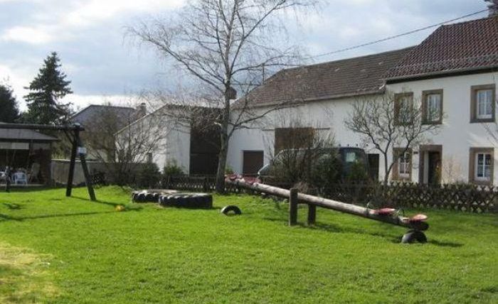 A well-maintained garden with a playground and a large lawn. In the background, several trees and a residential house can be seen.