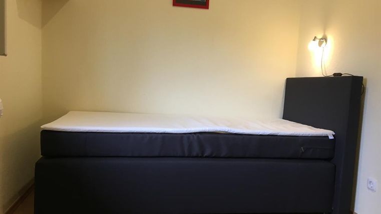 Une chambre simple avec un lit noir et un mur clair. Une petite lampe fournit l'éclairage.