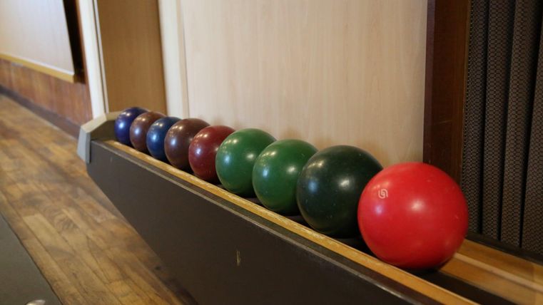 Een serie kleurrijke bowlingballen staat op een houten oppervlak. De ballen zijn in verschillende kleuren gerangschikt, waaronder blauw, groen, rood en bruin.