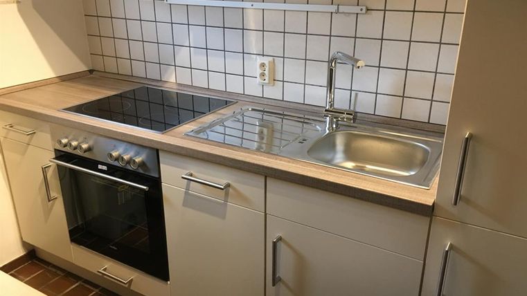 Une cuisine moderne avec une plaque de cuisson, un évier et un four. Les murs sont carrelés avec des carreaux blancs.