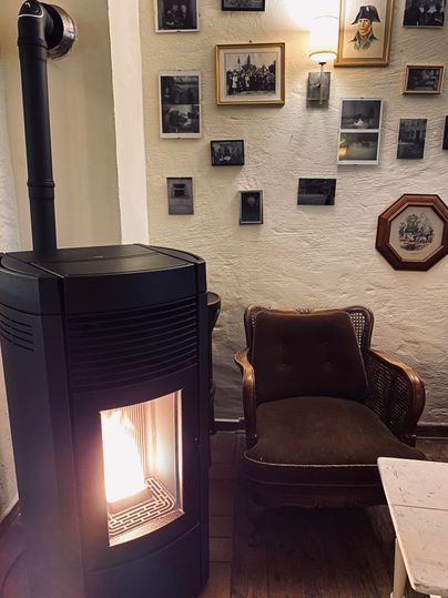 Un poêle à bois moderne se tient à côté d'un fauteuil confortable. Différentes images pendent au mur, créant une atmosphère nostalgique.