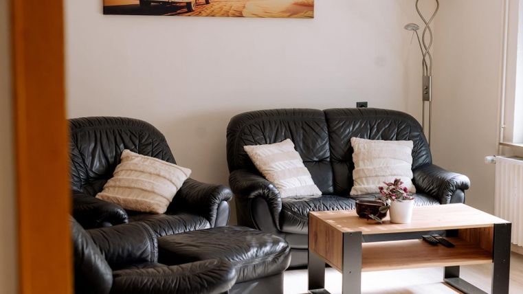 Ein gemütliches Wohnzimmer mit schwarzen Ledersofas und einem Holztisch. An der Wand hängt ein modernes Bild und es gibt eine Stehlampe.